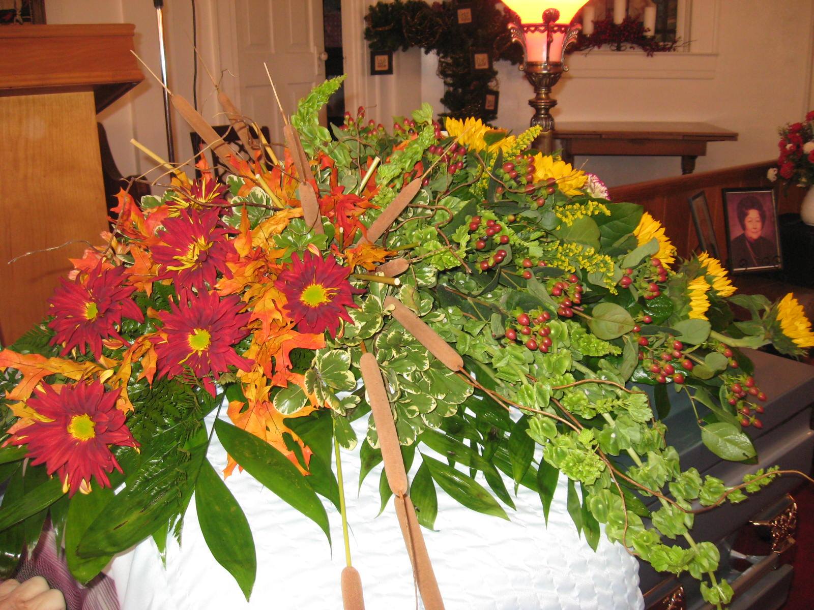 This half casket spray is made using a mixture of fall flowers designed a bit more modern in style. As seen in Picture, this would cover the lower half of the casket and drapes gracefully down toward the floor. Starting price as pictured is $350.00. Some of these flowers are seasonal so please call in to place an order and we will make as close as possible.